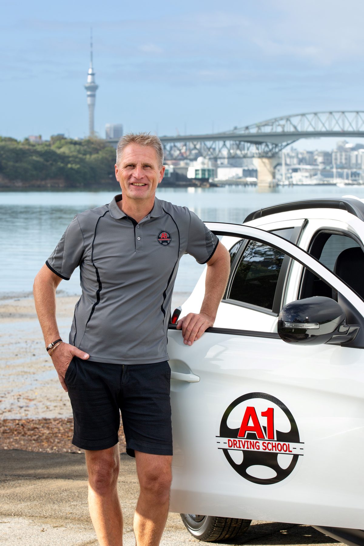 Harald from A1 Driving School beside a branded dual-controlled car on the Auckland waterfront